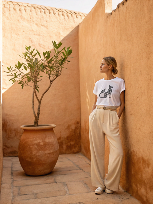 Woman standing in a sunlit courtyard with a potted plant and textured walls.