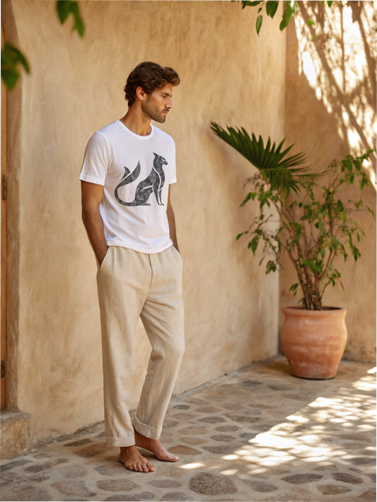 Man wearing a white t-shirt with a graphic design and beige pants standing in a sunlit outdoor setting.